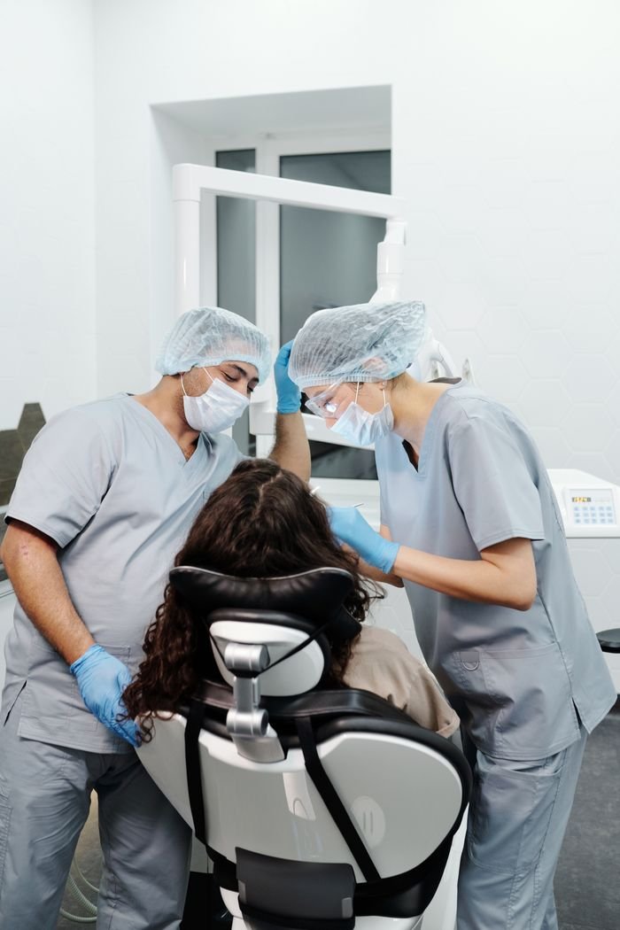Two dentists in scrubs and masks providing dental care to a patient in a clinic.